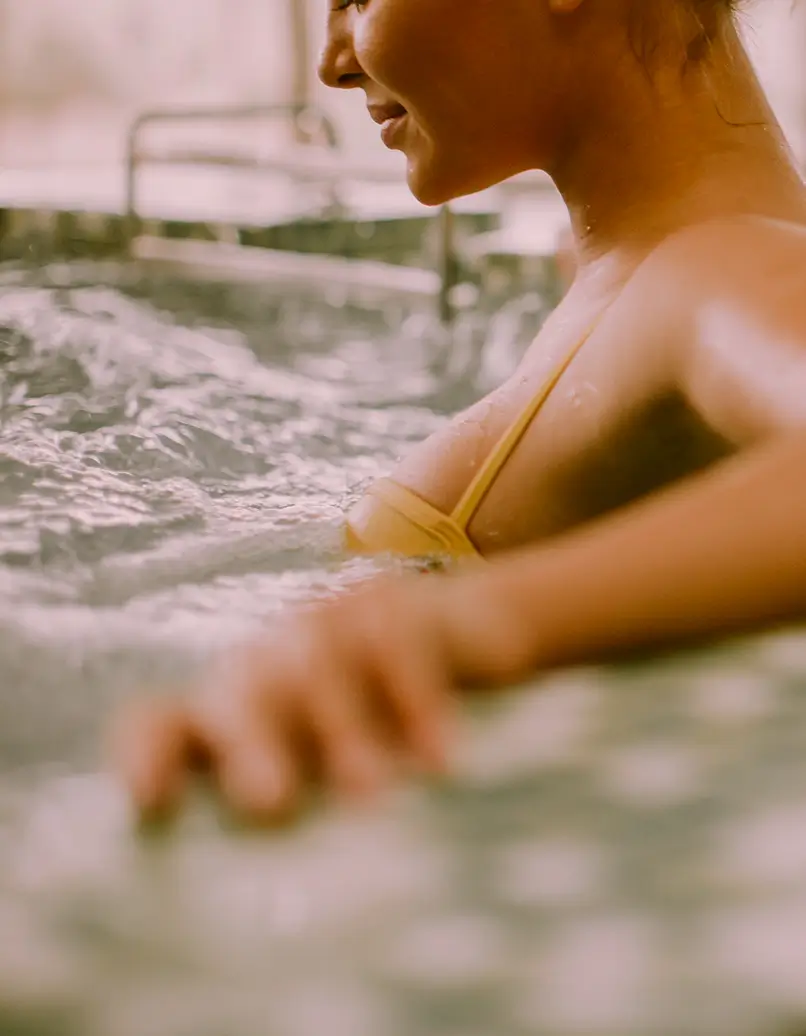 Person in a yellow bikini top relaxing in a pool, water splashing around them, side view.