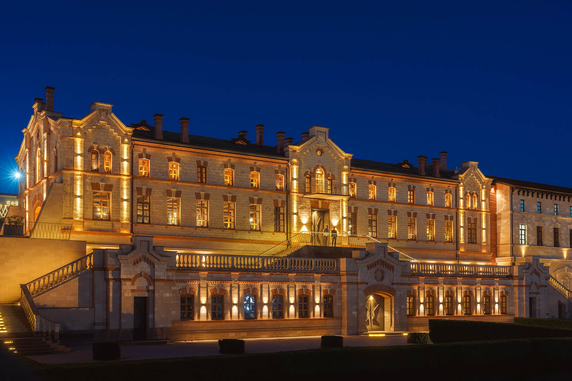 Historic stone building with ornate façade lit by warm exterior lights at night, clear dark blue sky above